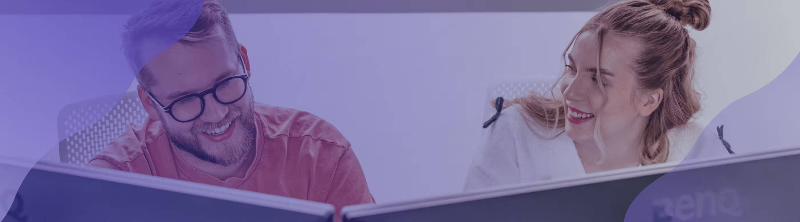 Two people smiling and looking at monitors